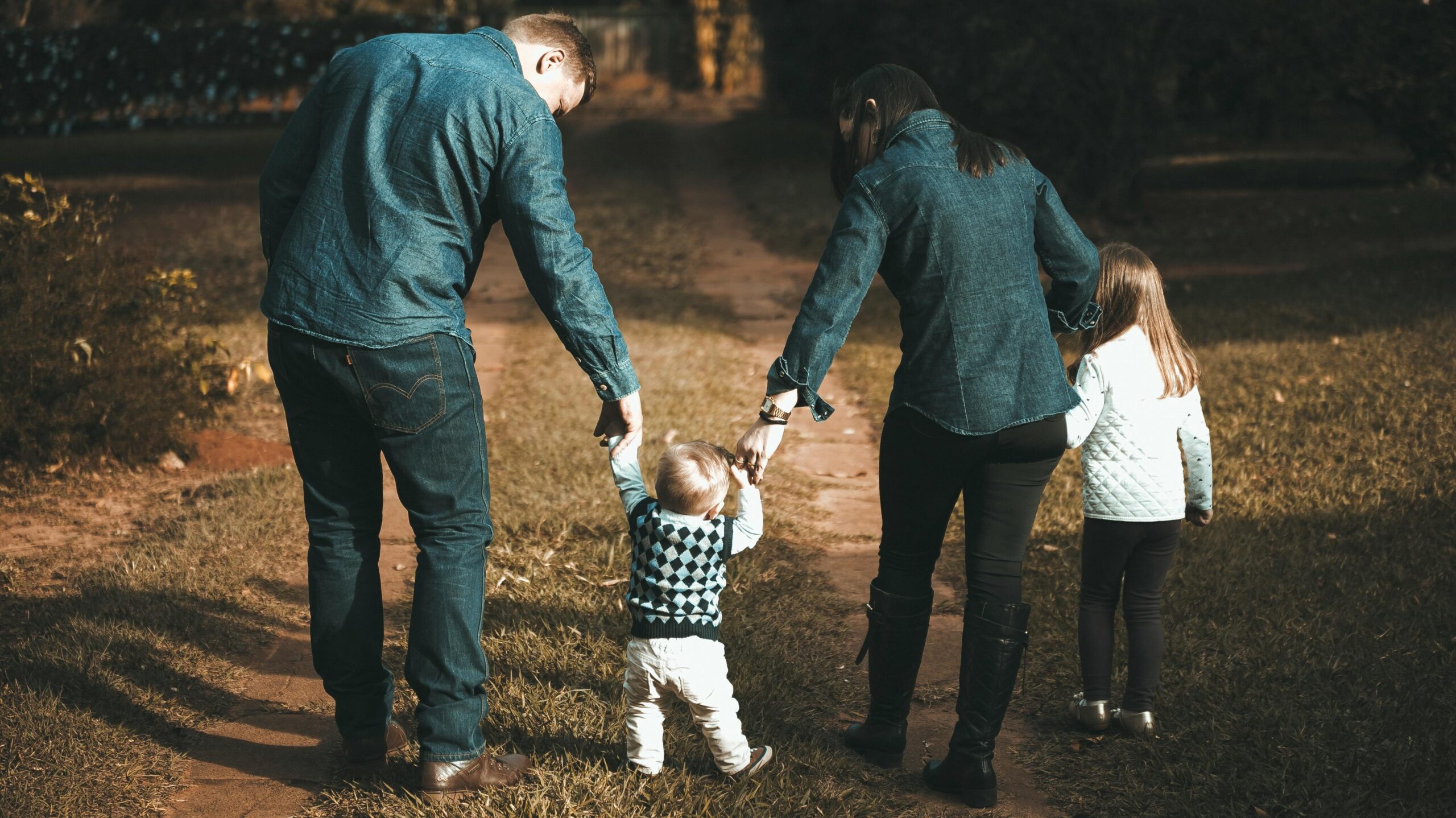 A family of four walks hand in hand on a path, enjoying a sunny day outdoors.