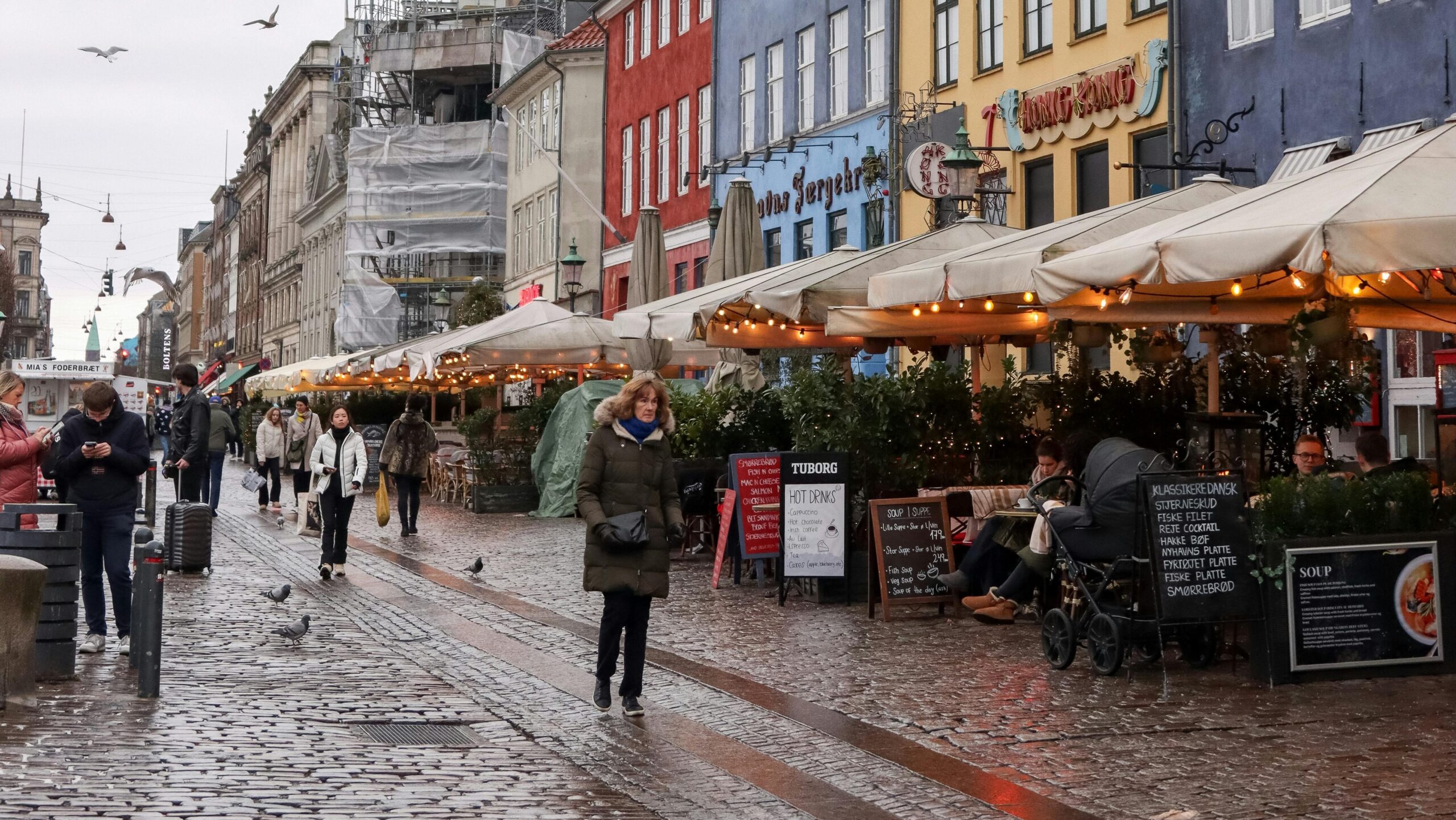 Vibrant Nyhavn in Copenhagen with colorful buildings and bustling street life on a cloudy day.