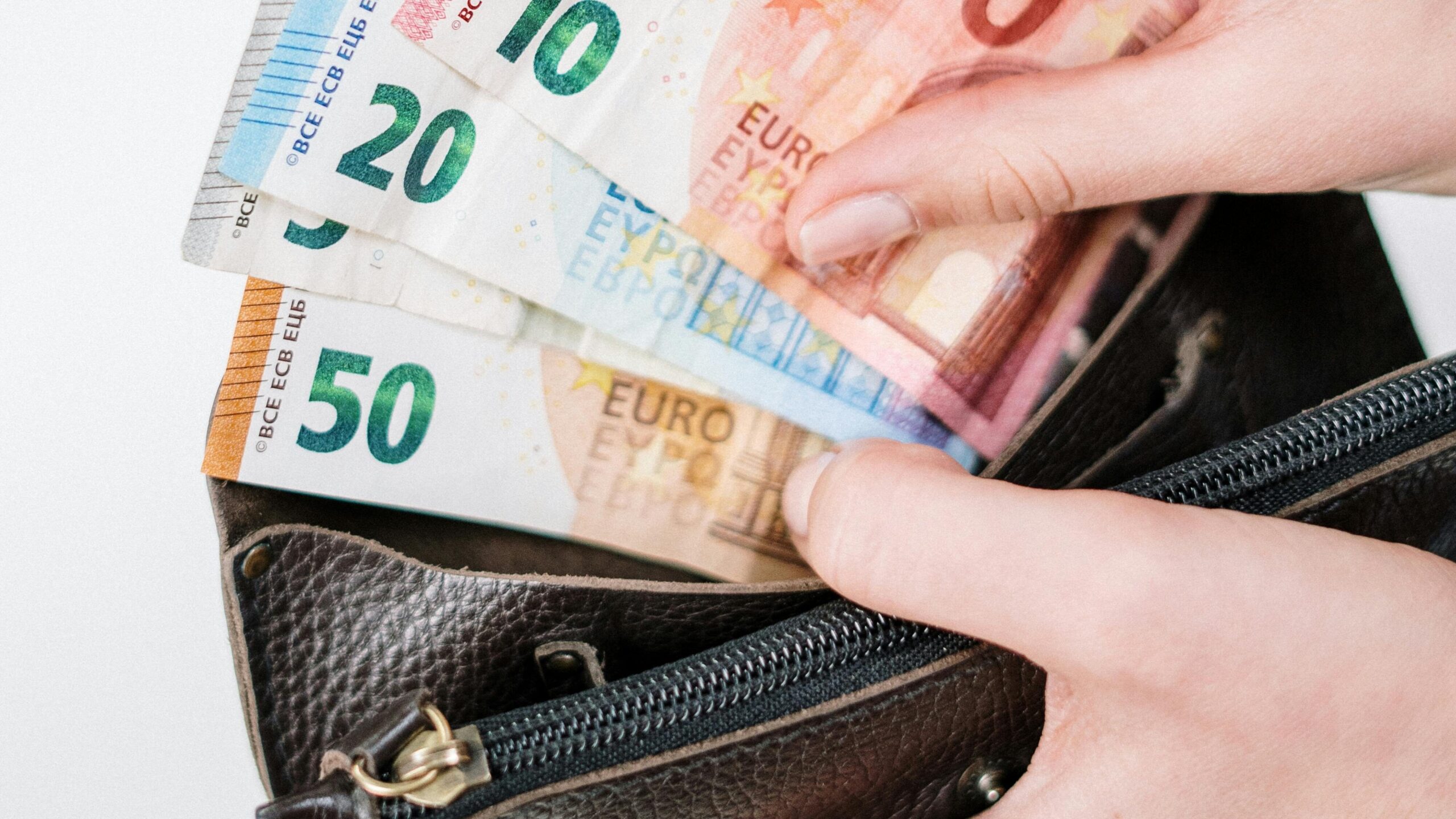 Close-up of a hand holding euro banknotes of different denominations, taken from a black wallet.