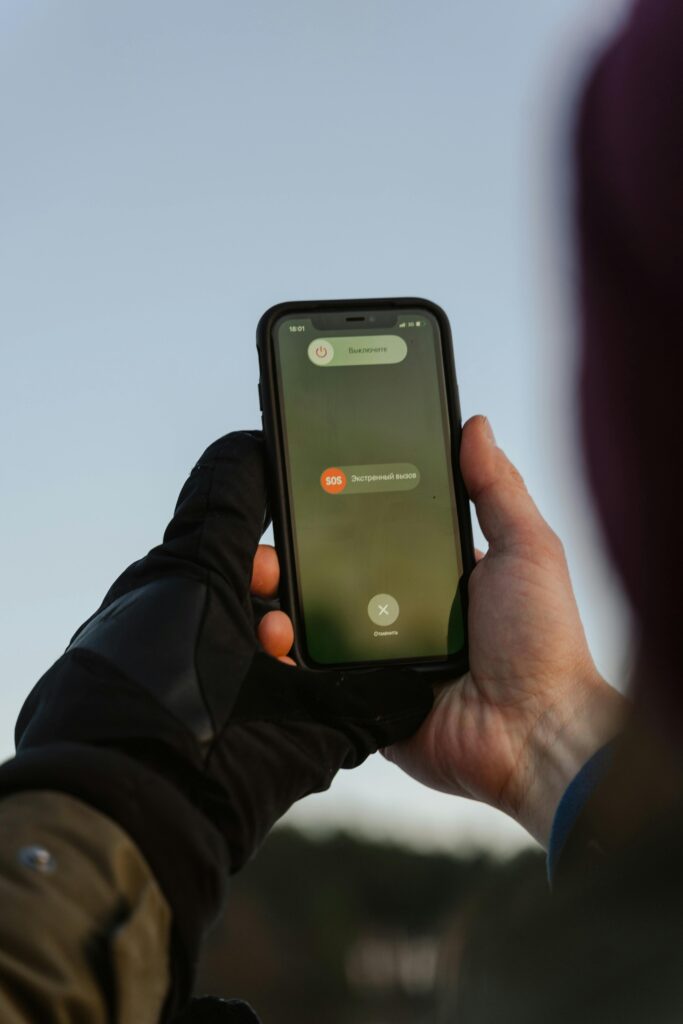 Person with gloves holding smartphone displaying emergency call option outdoors