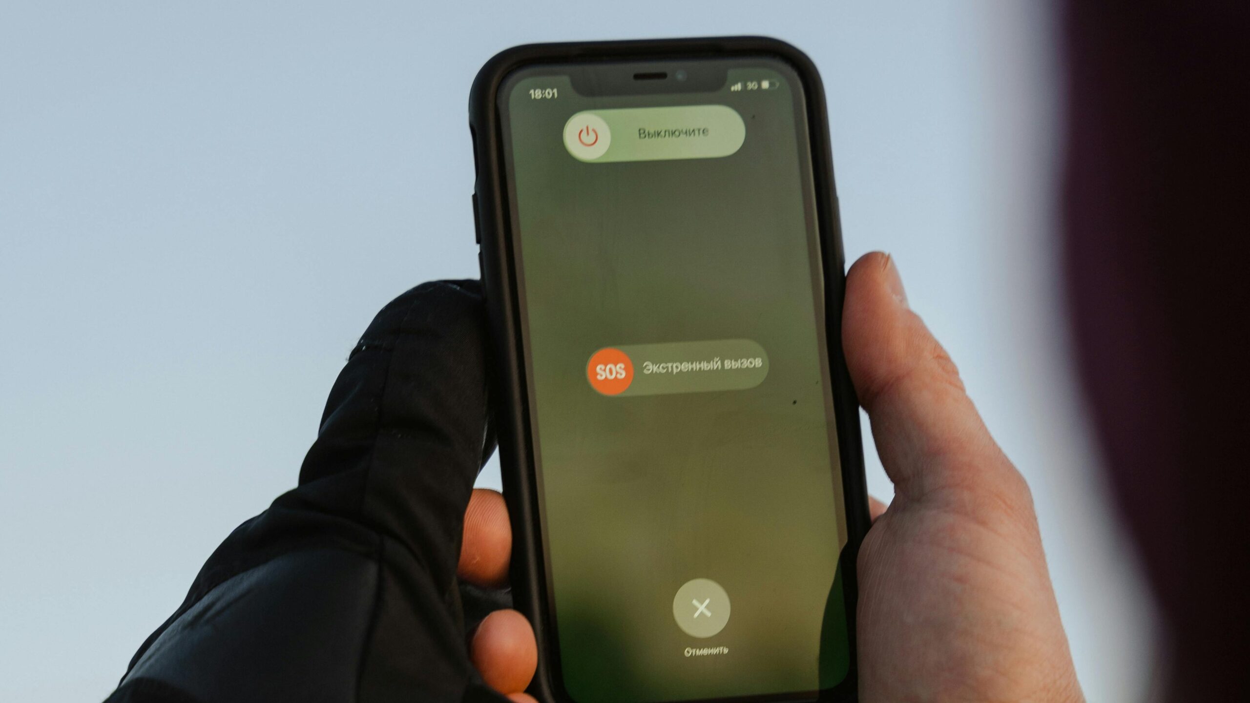 Person with gloves holding smartphone displaying emergency call option outdoors