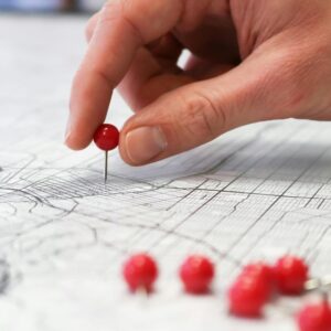 Close-up of a hand placing a red pin on a map indicating geographic location pinning.